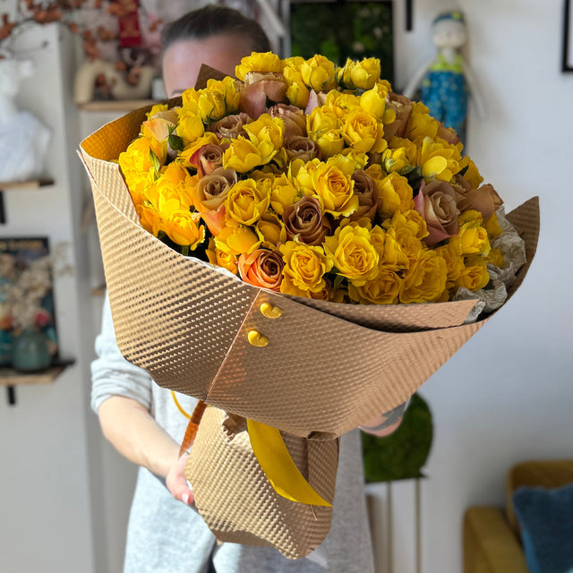 Big bouquet of yellow roses held by woman.