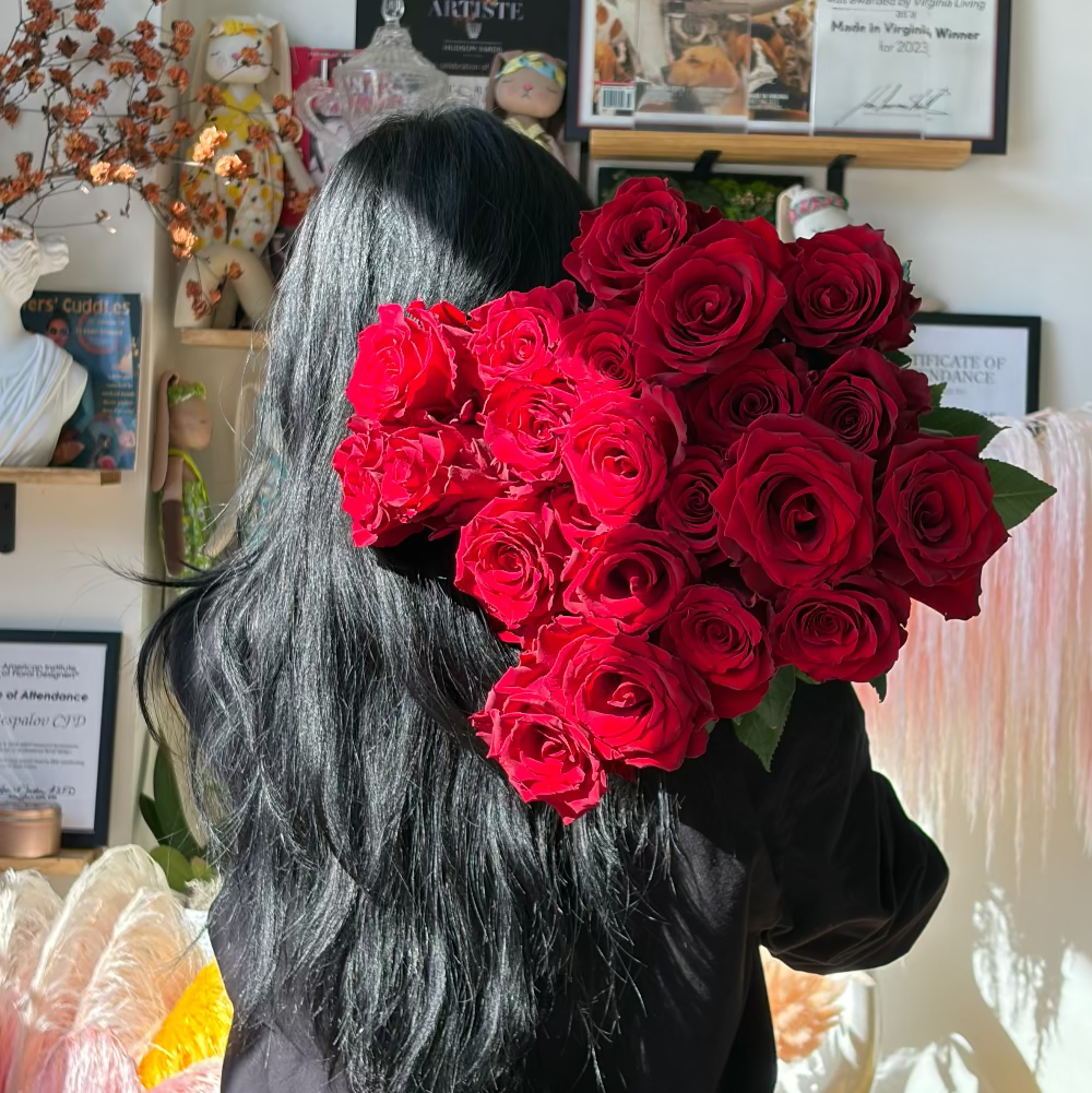 Person holding a large bouquet of red roses in an indoor setting with decor and framed items on the wall.