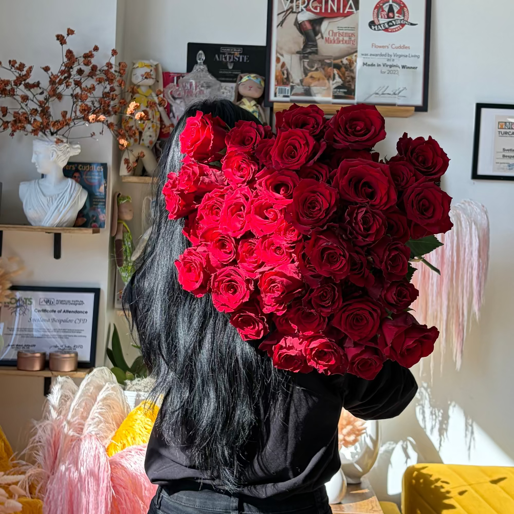 Person holding a large bouquet of red roses in a room with decor elements.