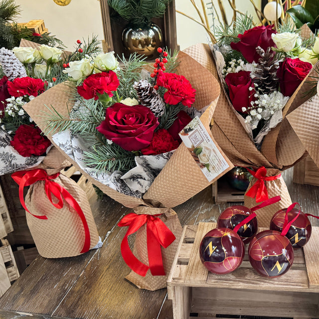 Bouquets of red roses with greenery on a wooden table, surrounded by festive decorations.