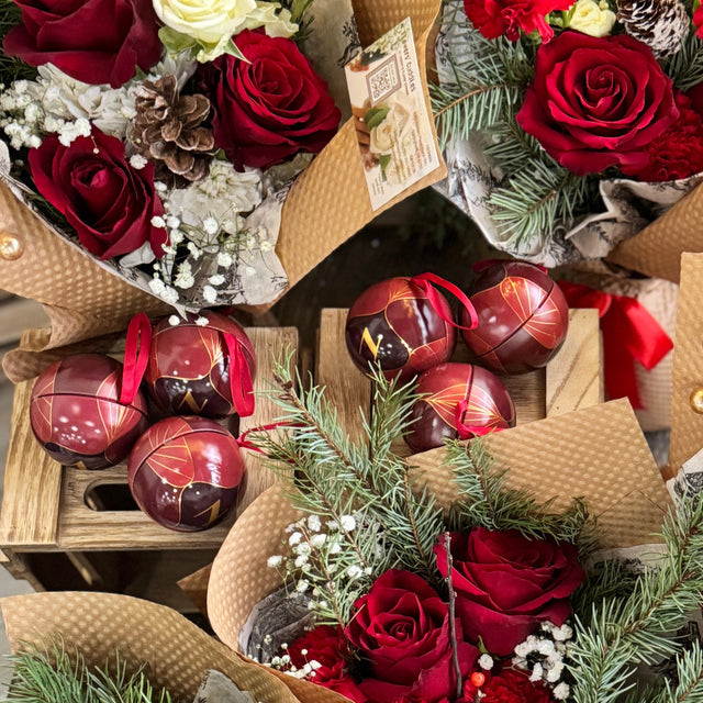 Bouquets of red and white flowers with decorative ribbons and small gift bags on a wooden surface.