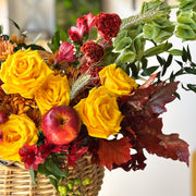 Yellow roses and seasonal chrysanthemums with autumn foliage in a natural woven basket