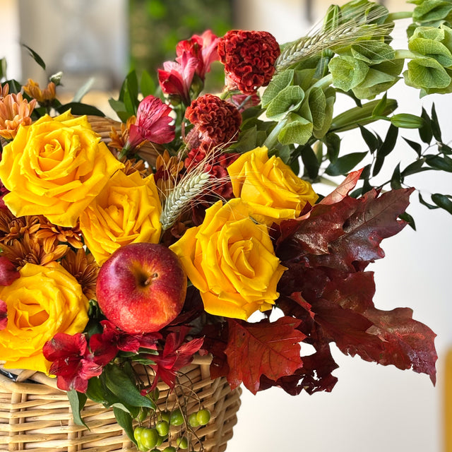 Yellow roses and seasonal chrysanthemums with autumn foliage in a natural woven basket
