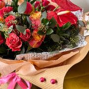 Eco-wrapped Urban Bloom bouquet with roses, anthuriums, and eucalyptus tied in kraft paper and tissue.