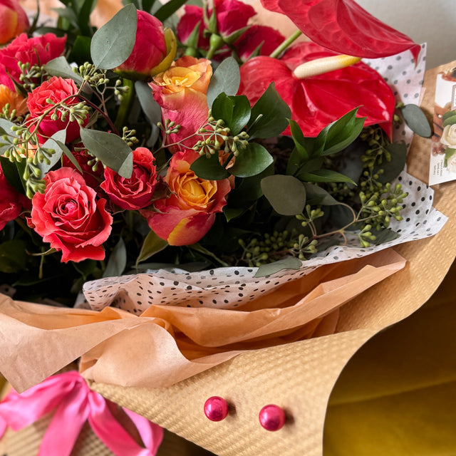 Eco-wrapped Urban Bloom bouquet with roses, anthuriums, and eucalyptus tied in kraft paper and tissue.