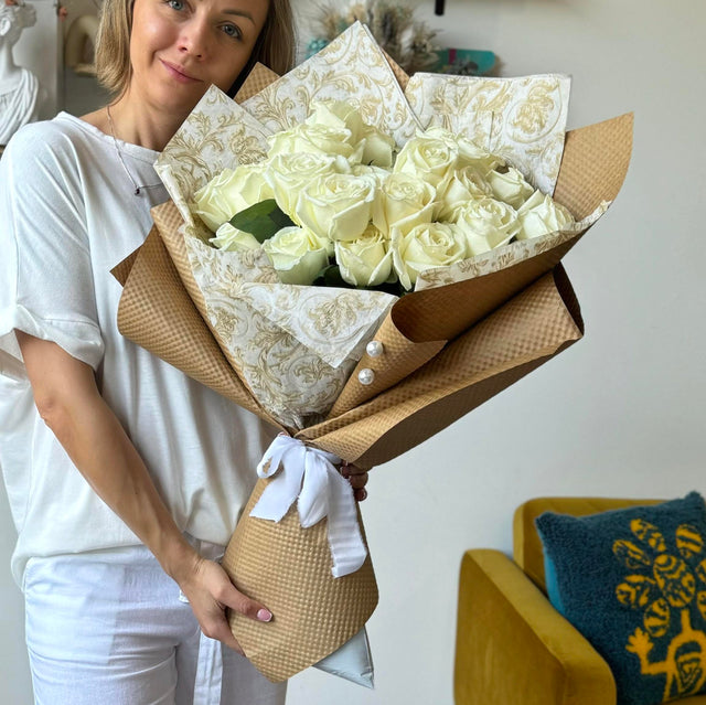 Florist holding a bouquet of elegant white roses, wrapped in kraft paper with white ribbon and bead details, showcasing a classic and timeless floral arrangement.