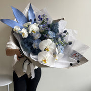 bouquet with orchids, delphinium, and painted foliage in soft blue 