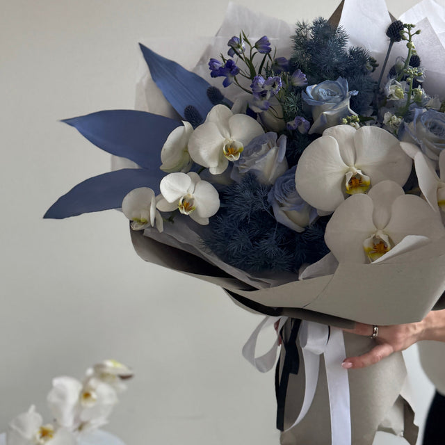 Chic bouquet with painted foliage, delphinium, and orchids