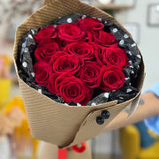 Bouquet of red roses wrapped in brown paper with black polka dots on a blurred indoor background