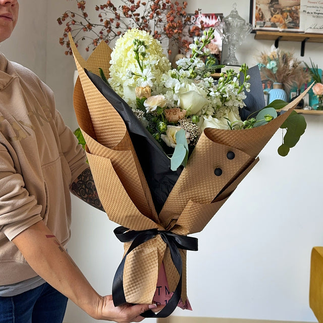 Florist is holding beautiful bouquet of white flowers, wrapped in black tissue and kraft paper.