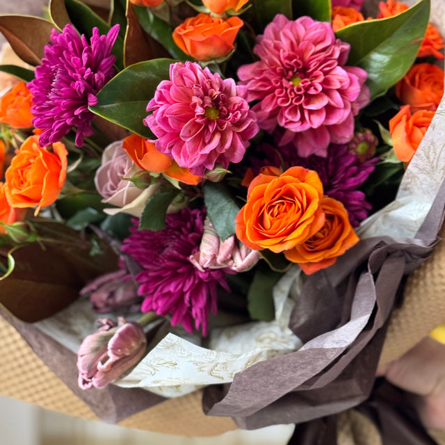 Bouquet of flowers with orange and pink flowers wrapped in brown paper.