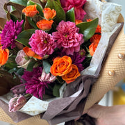 Bouquet of flowers with pink, orange, and purple colors wrapped in brown paper.
