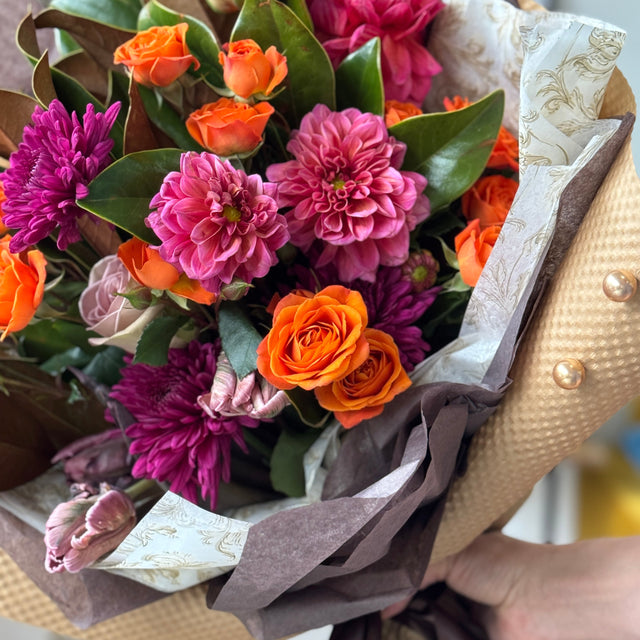 Bouquet of flowers with pink, orange, and purple colors wrapped in brown paper.