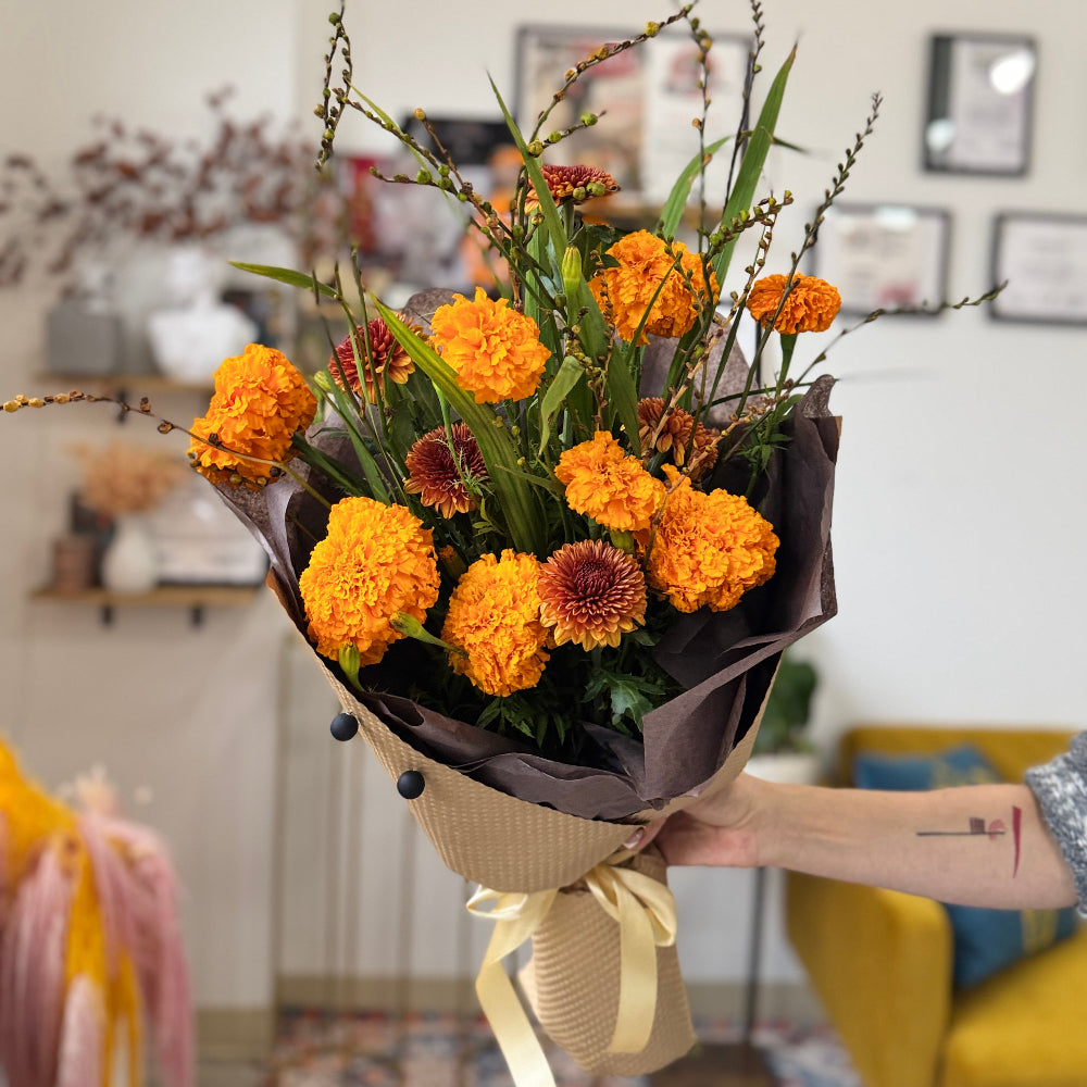 Bouquet of orange and brown flowers held by a person in a room with decor elements.