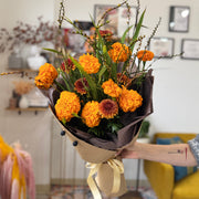 Bouquet of orange and brown flowers held by a person in a room with decor elements.