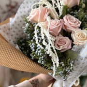 Bouquet of pink  roses with greenery held by a person.