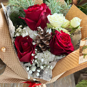 Bouquet of red and white roses with pinecones and greenery in brown paper wrapping.