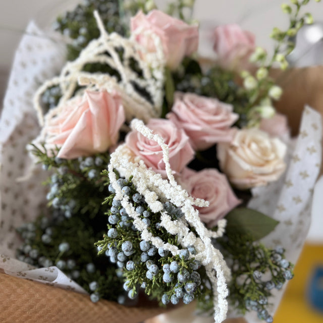 Bouquet of pink roses with greenery in a brown paper wrap.