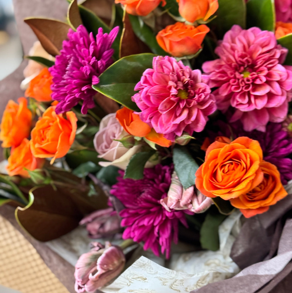 Bouquet of flowers with orange, pink, and purple colors in a brown paper wrap.