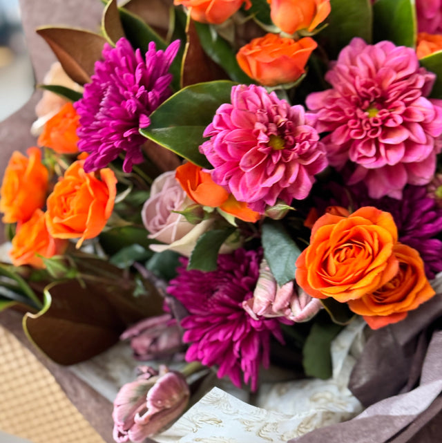 Bouquet of flowers with orange, pink, and purple colors in a brown paper wrap.