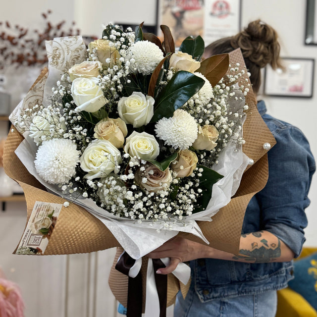 Rustic Magnolia Mist bouquet with white blooms, magnolia foliage, and baby’s breath, arranged in a soft, natural style.