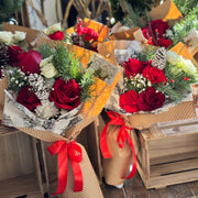 Bouquets of red and white flowers with greenery, wrapped in brown paper and red ribbons, displayed on a wooden surface.