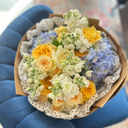 Cheerful flower arrangement of yellow roses, white stock, and blue hydrangea