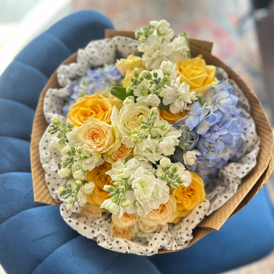 Cheerful flower arrangement of yellow roses, white stock, and blue hydrangea