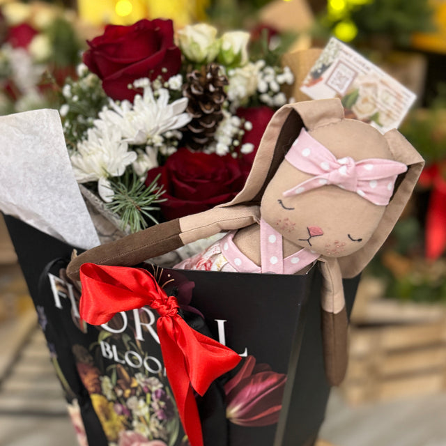 Floral arrangement with a plush toy and decorative bow in a black box labeled 'Floral Blooms'.