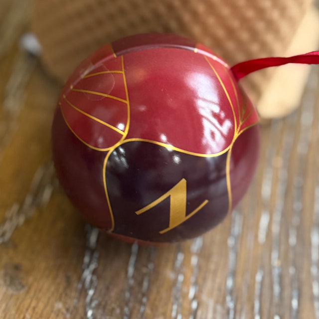 Red ornament with gold design and number 1 on a wooden surface