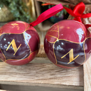 Two red ornaments with gold letter 'N' on a wooden surface