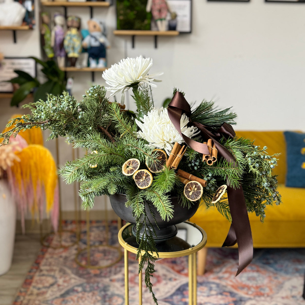 Decorative floral arrangement with greenery and white flowers on a gold stand in a room setting.