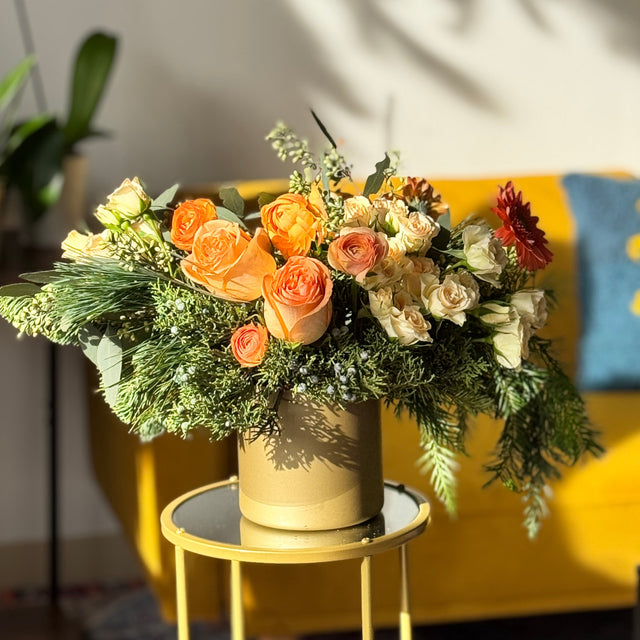 Christmas table arrangement with coral roses, cream spray roses, and evergreen accents