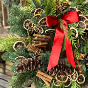 Decorative Christmas wreath with pine cones, cinnamon sticks, and a red ribbon on a wooden crate.