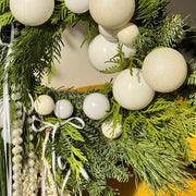 Christmas wreath with white ornaments and greenery on a blurred background