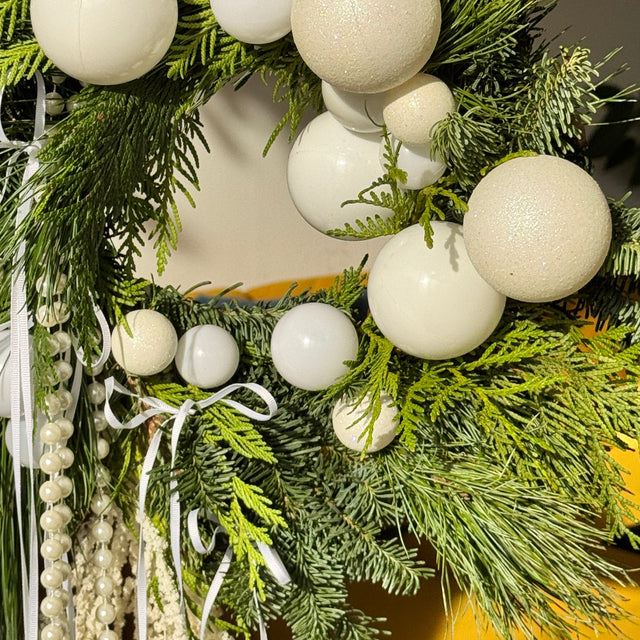 Christmas wreath with white ornaments and greenery on a blurred background