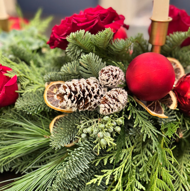 Close-up of evergreen centerpiece with red roses and pinecones