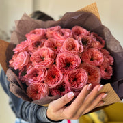 Close-up of a florist holding a bouquet of coral roses with large, fluffy heads and dark green centers, showcasing its stunning detail.