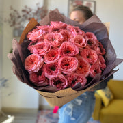 Full view of a bouquet of coral roses with large, fluffy heads and dark green centers, wrapped in elegant brown tissue paper.