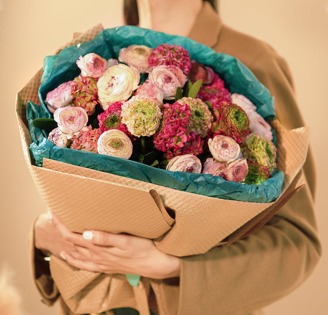 Bouquet of ranunculus wrapped in Kraft paper in the hands of a girl