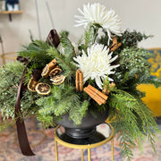 Decorative floral arrangement with white flowers and greenery on a small round table in a living room.