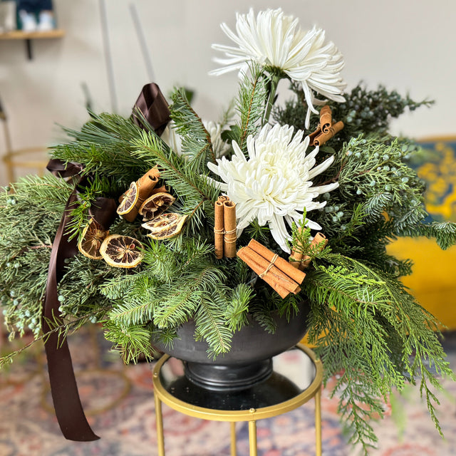 Decorative floral arrangement with white flowers and greenery on a small round table in a living room.