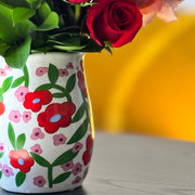 Decorative vase with floral design containing red and pink flowers on a wooden surface.