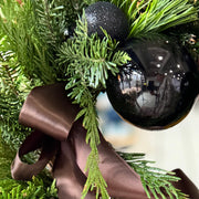 Decorative wreath with black ornaments, and a brown ribbon on a blurred background.