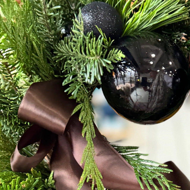Decorative wreath with black ornaments, and a brown ribbon on a blurred background.