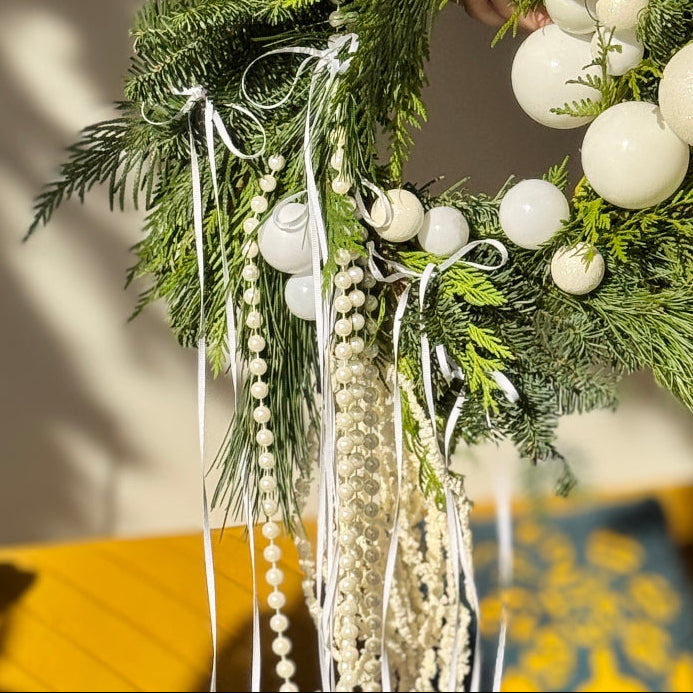 Decorative wreath with white spherical ornaments and greenery on a neutral background