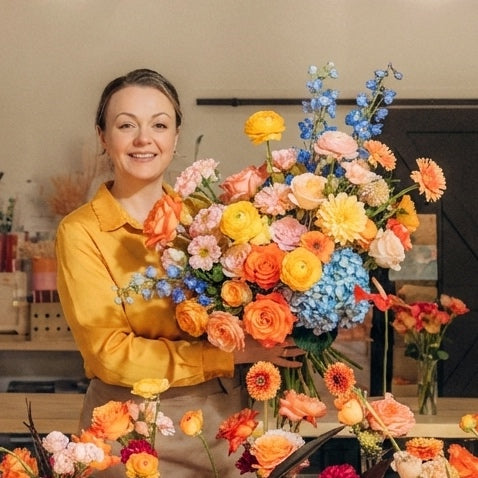 Person holding a large arrangement of colorful flowers in a floral shop.