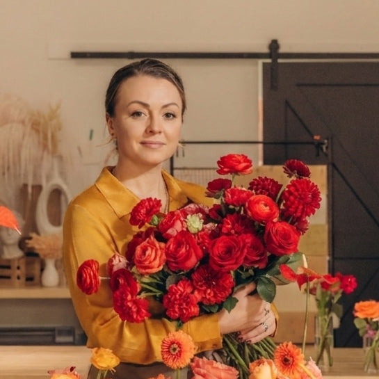 Woman holding a bouquet of red flowers in a floral shop setting