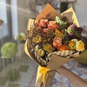 Beautiful fall-colored bouquet wrapped in kraft paper, held in hand.