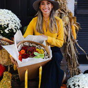 Fall bouquet of flowers with mums, roses, and anthurium in a box, held by a woman in a yellow blouse.